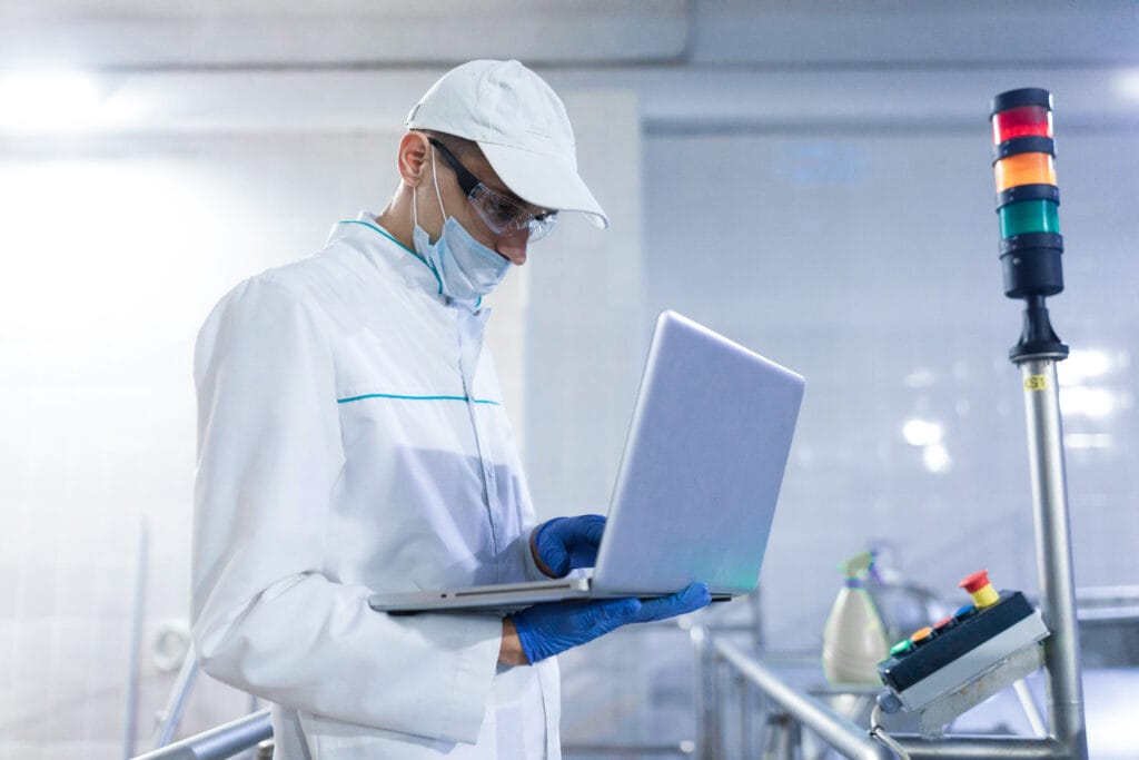 technologist with laptop in his hands make a set up of the production line while standing at the department of dairy factory